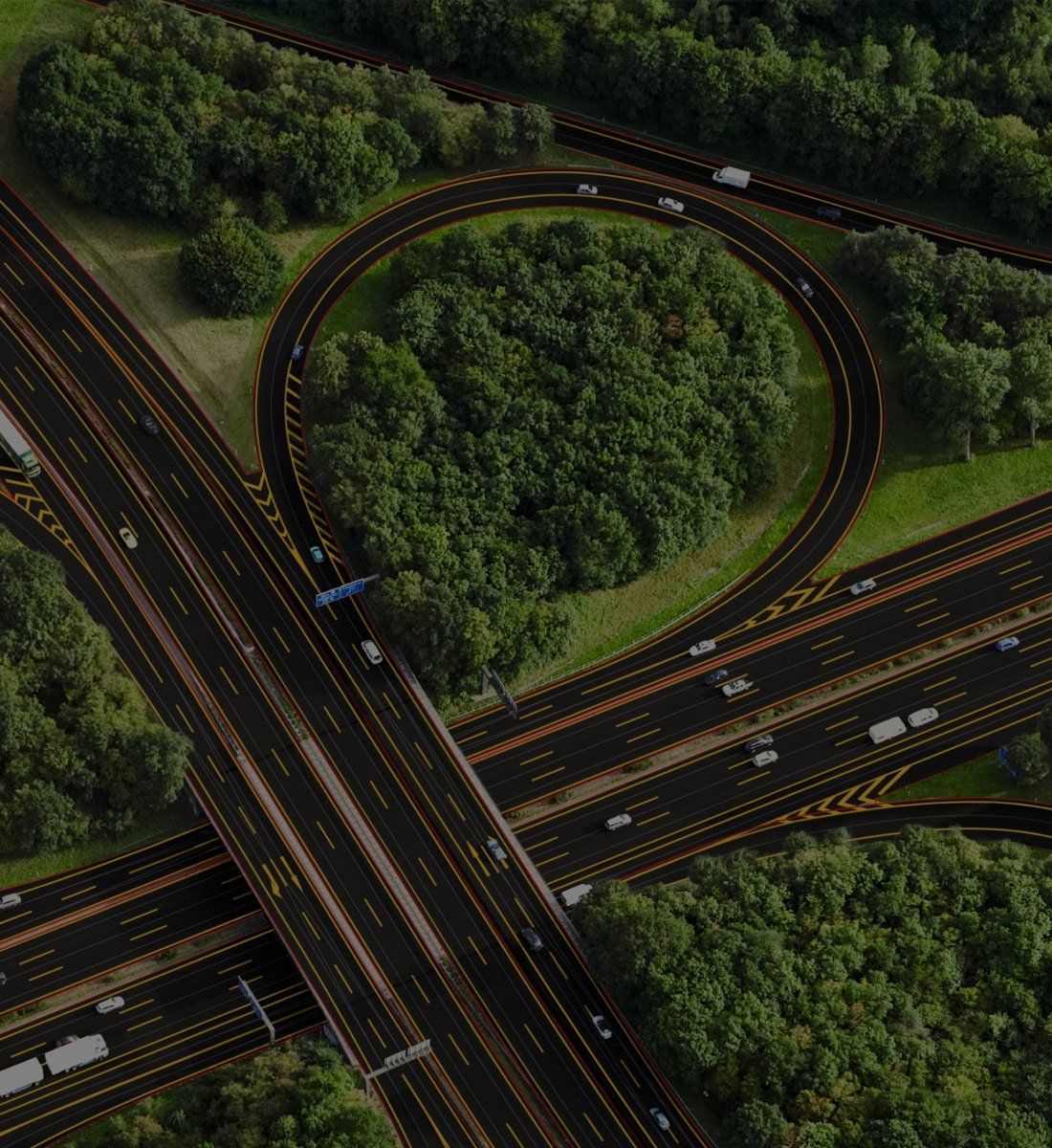 Aerial view of a highway interchange surrounded by dense green trees, featuring multiple lanes and vehicles in motion.