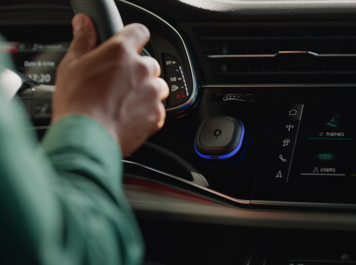 Person driving a car, focusing on the dashboard showing various controls and a screen with app icons and settings.