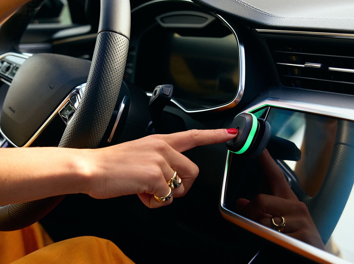 A hand pressing a green-lit button on a car's dashboard, near the steering wheel, inside a modern vehicle.
