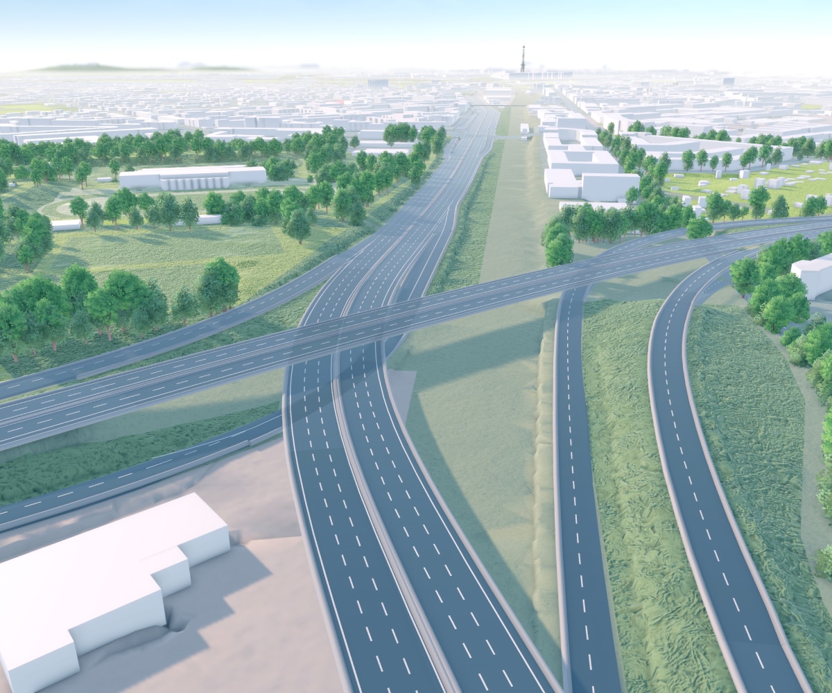 Aerial view of a highway interchange with multiple lanes, surrounded by lush greenery and scattered buildings under a clear sky.