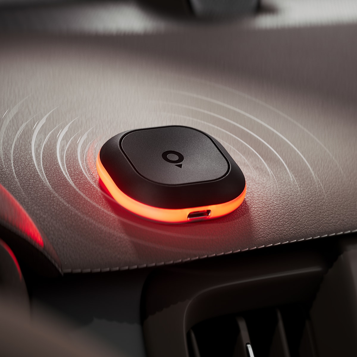 A black, square-shaped wireless Tom by TomTom device with a glowing red edge on a car dashboard, emitting circular signal waves.