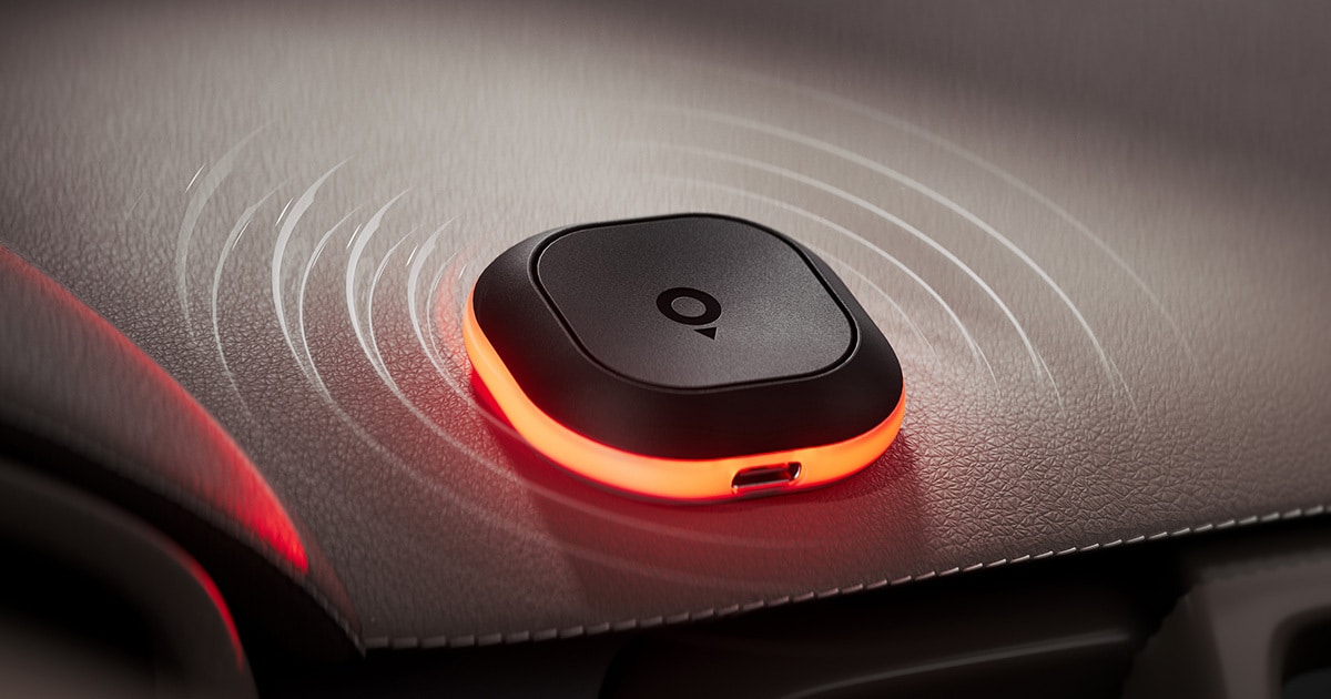 Tom by TomTom device with a glowing red base emits sound waves on a textured surface.