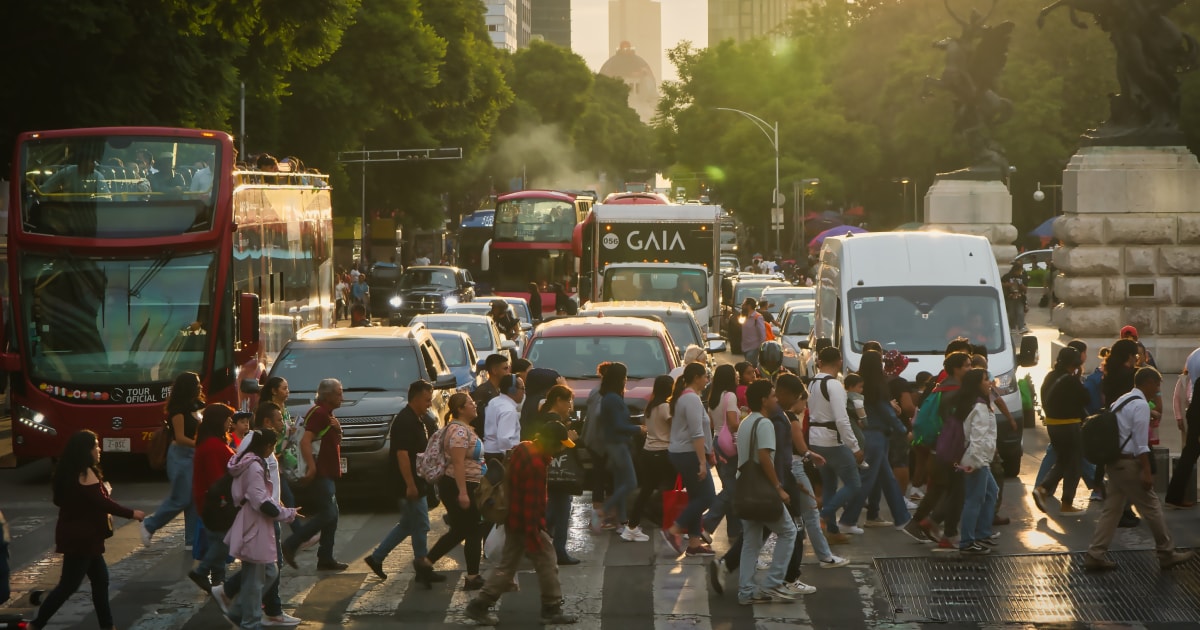 A busy zebra crossing in Mexico city with people crossing the street while vehicles ranging from buses to vans to cars wait
