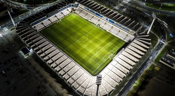 An aerial view of a well-lit football stadium at night, showcasing a pristine green pitch surrounded by seating areas.