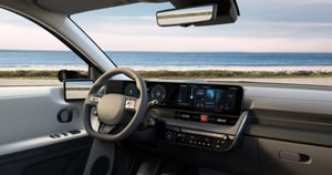 Modern car interior with sleek dashboard, digital displays, and steering wheel, overlooking a scenic ocean view through the windshield.