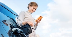 Woman succesfully charging her EV looking at her phone smiling