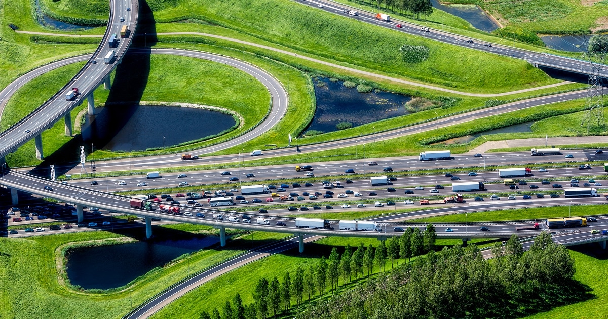 Aerial view of a multi-level highway interchange with heavy traffic surrounded by lush green landscapes and small ponds.