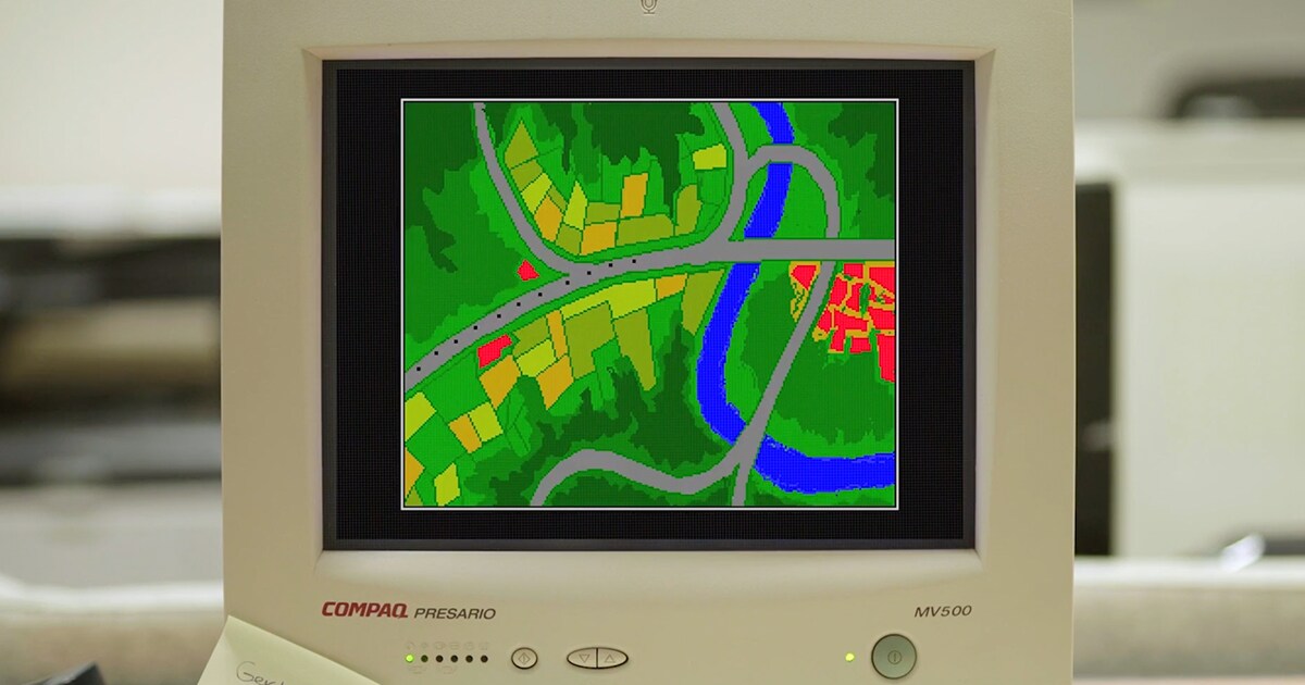 Vintage monitor displaying a colorful, pixelated map with roadways, fields, and a river, showcasing an early example of digital cartography.