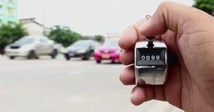 A hand holding a click counter to count cars