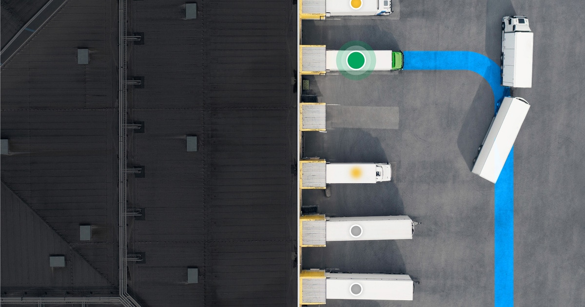 Aerial view of a distribution center with trucks parked at loading bays, one highlighted in green. A blue path guides trucks on the asphalt.