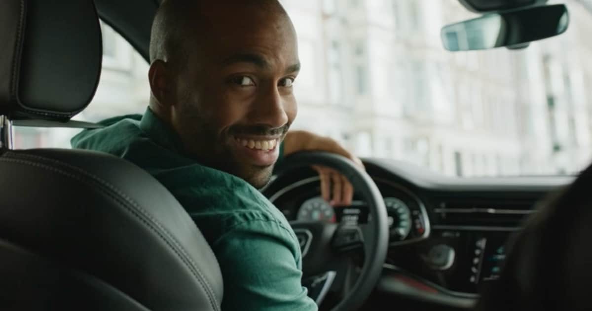 Man smiling while sitting in a car, looking back over his shoulder.