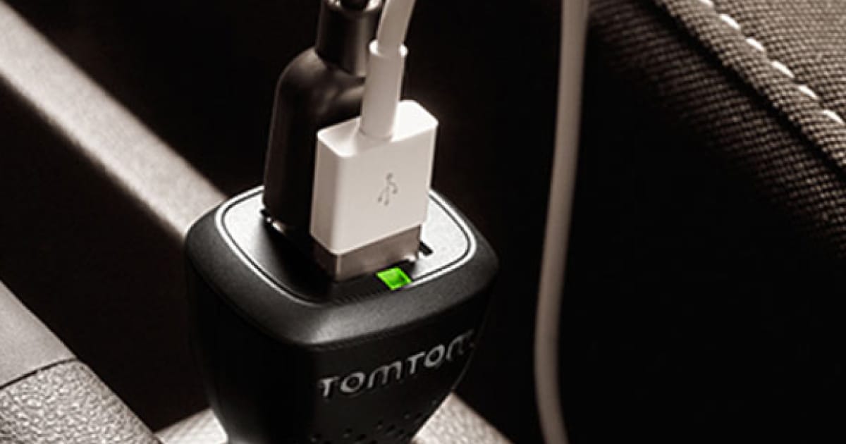 Close-up of a USB cable plugged into a car charger labeled "TomTom," inserted into a car's power outlet.