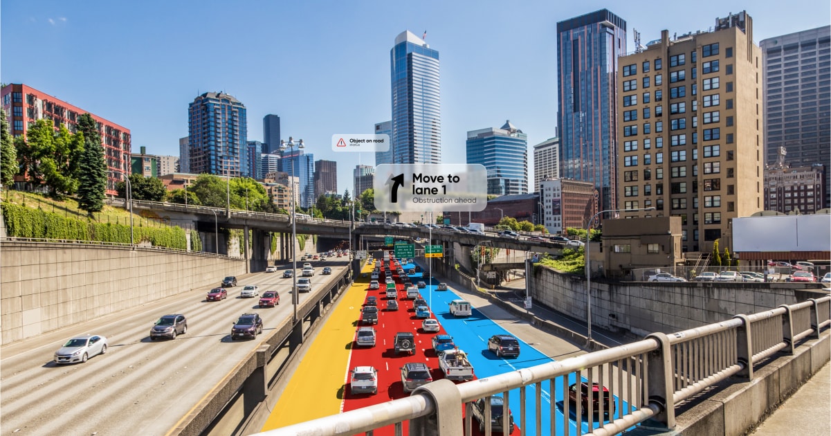 A busy highway scene with traffic and navigation alerts to "Move to lane 1" due to an obstruction, framed by city skyscrapers.