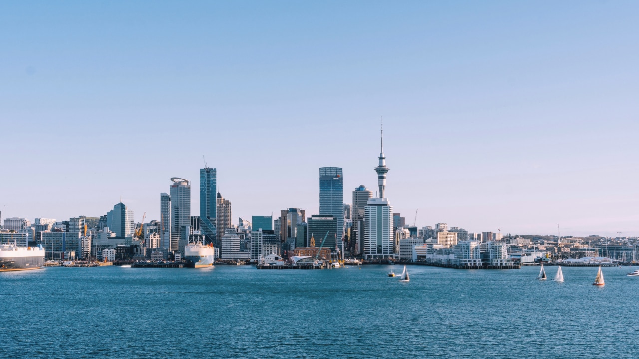 Scenic view of Auckland's skyline from the water, showcasing modern buildings and the Sky Tower under clear blue skies.