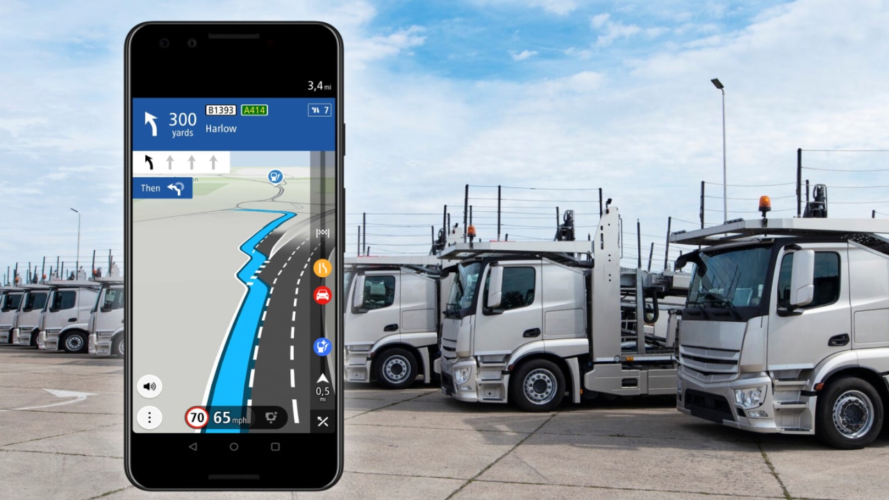 Smartphone displaying GPS navigation in front of parked trucks, showing a route with distance and speed limit.