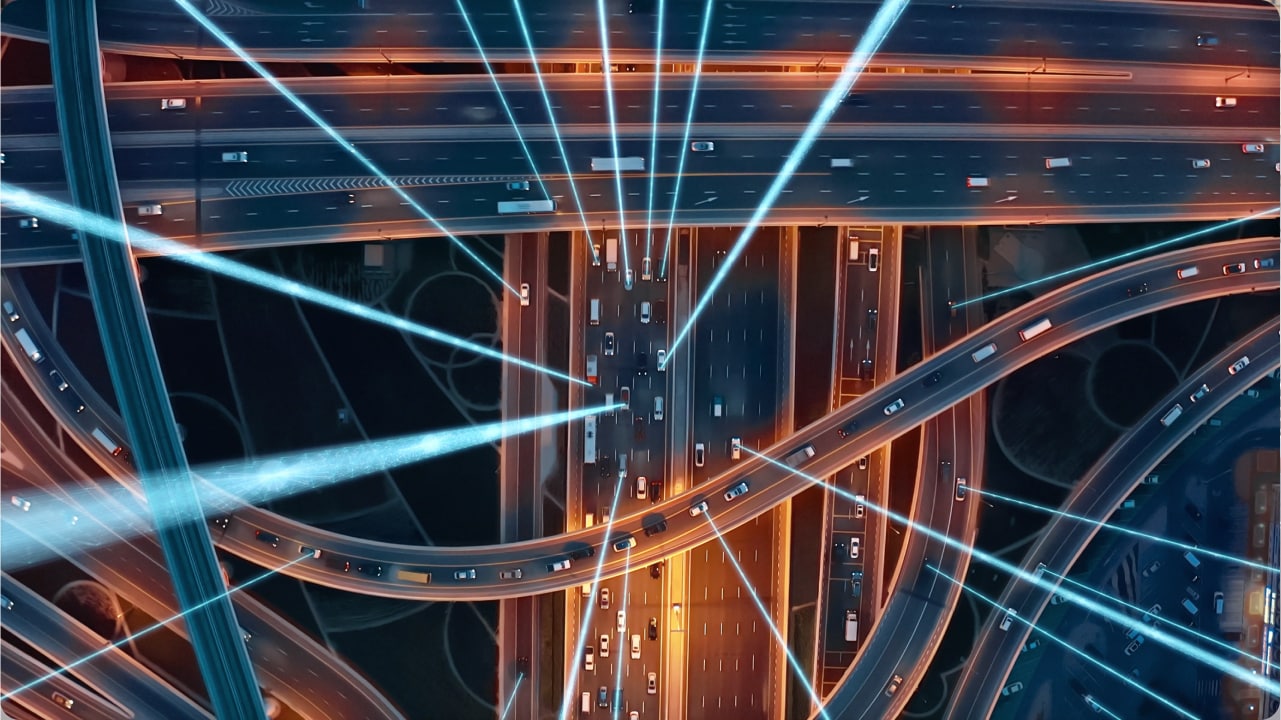 Aerial view of a busy highway interchange at night with light trails and blue lines, creating a futuristic, dynamic scene.
