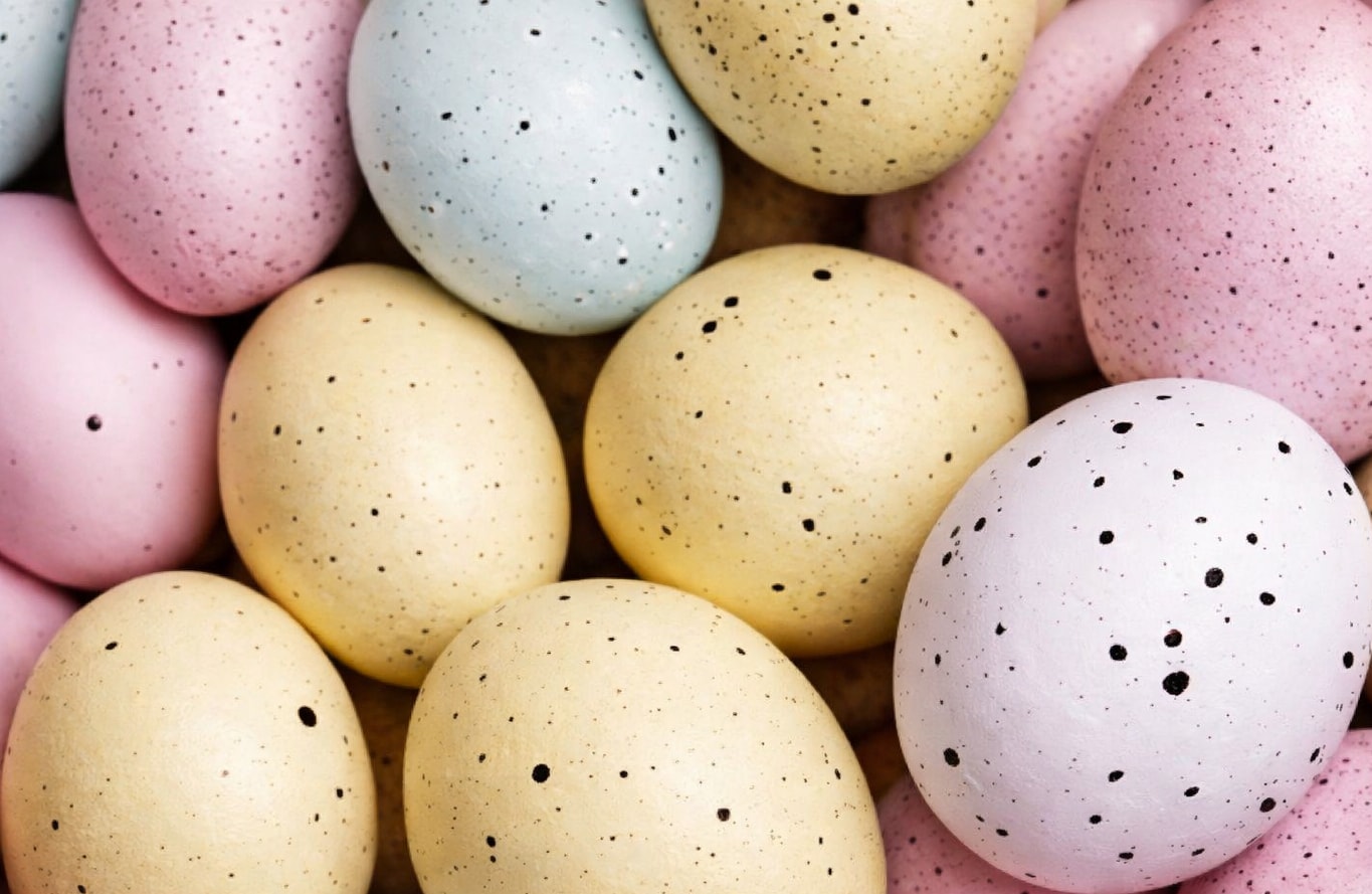 A pile of colorful, speckled Easter eggs in pastel shades of pink, yellow, and blue.