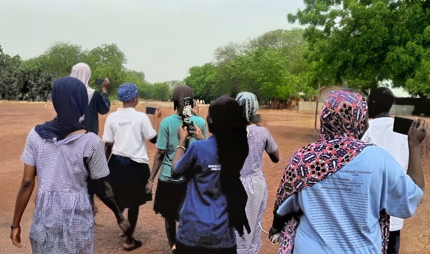 A group of people walking away, holding smartphones, in a natural outdoor setting with greenery and a dirt path.