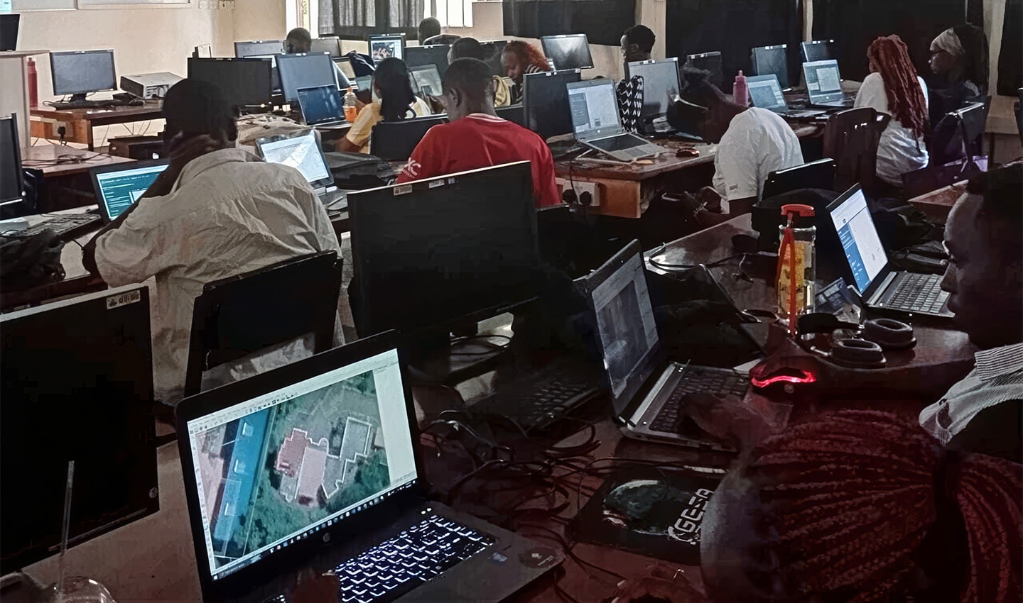 A computer lab filled with students working on laptops, with various screens displaying maps and data.