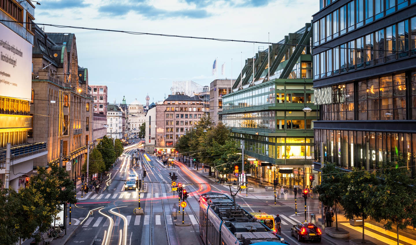 A street in Sweden with multiple modes of transport such as cars, trams, two-wheelers etc