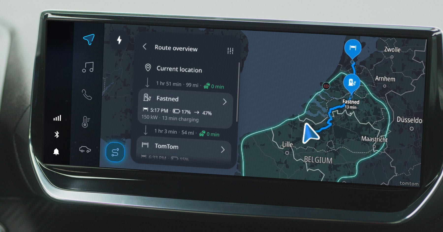 Car navigation screen showing a route through Belgium, highlighting a Fastned charging station with a detailed route overview and distance information.