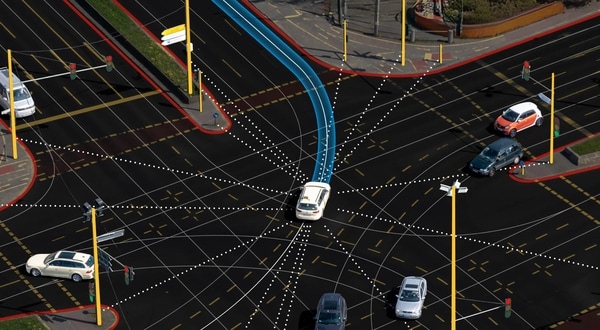 Aerial view of a city intersection with multiple cars, traffic lights, and digital navigation paths indicated by lines and dots.