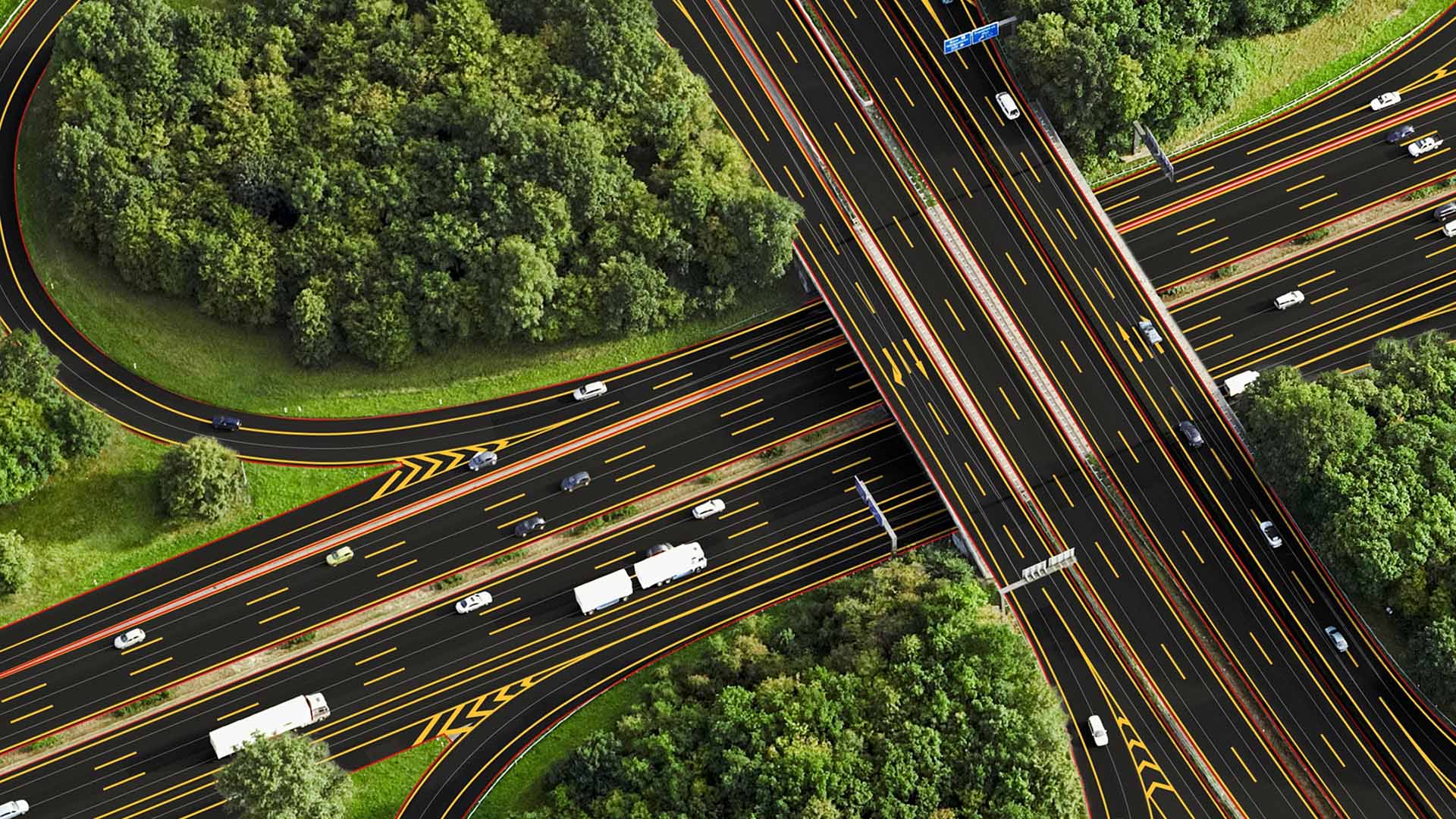 Aerial view of a highway interchange with multiple lanes and vehicles surrounded by lush green trees.