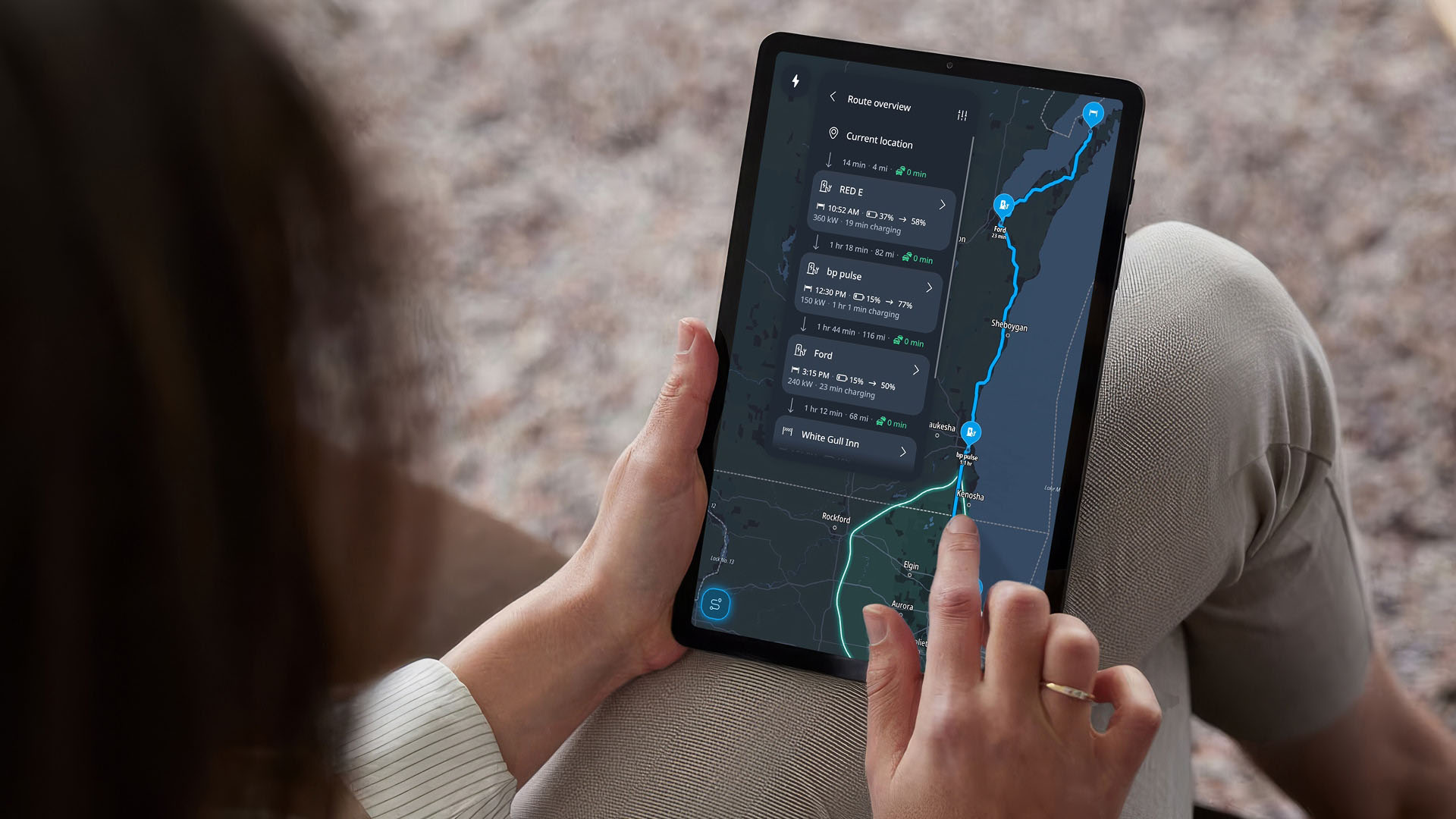 Person holding a tablet displaying a navigation app with a route map and charging station information.