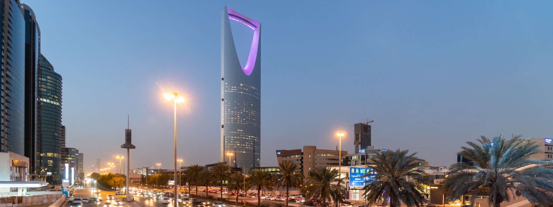 City street in Riyadh at dusk, featuring the illuminated Kingdom Centre Tower.