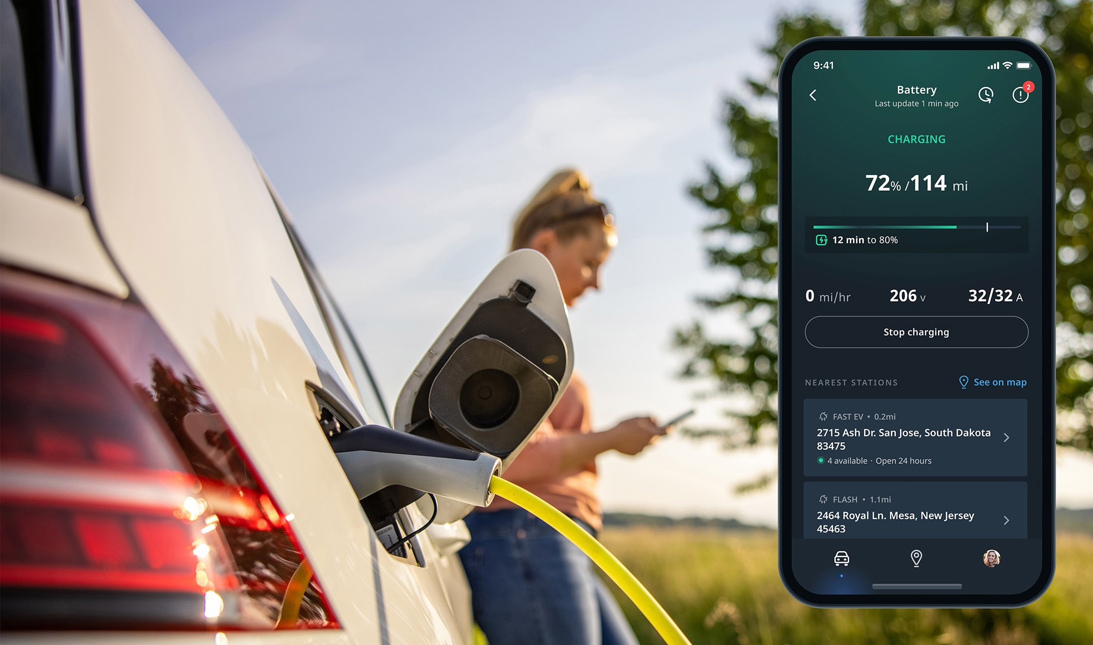 Electric car charging with a yellow cable in a rural area; a person in the background uses a smartphone app displaying charging details.