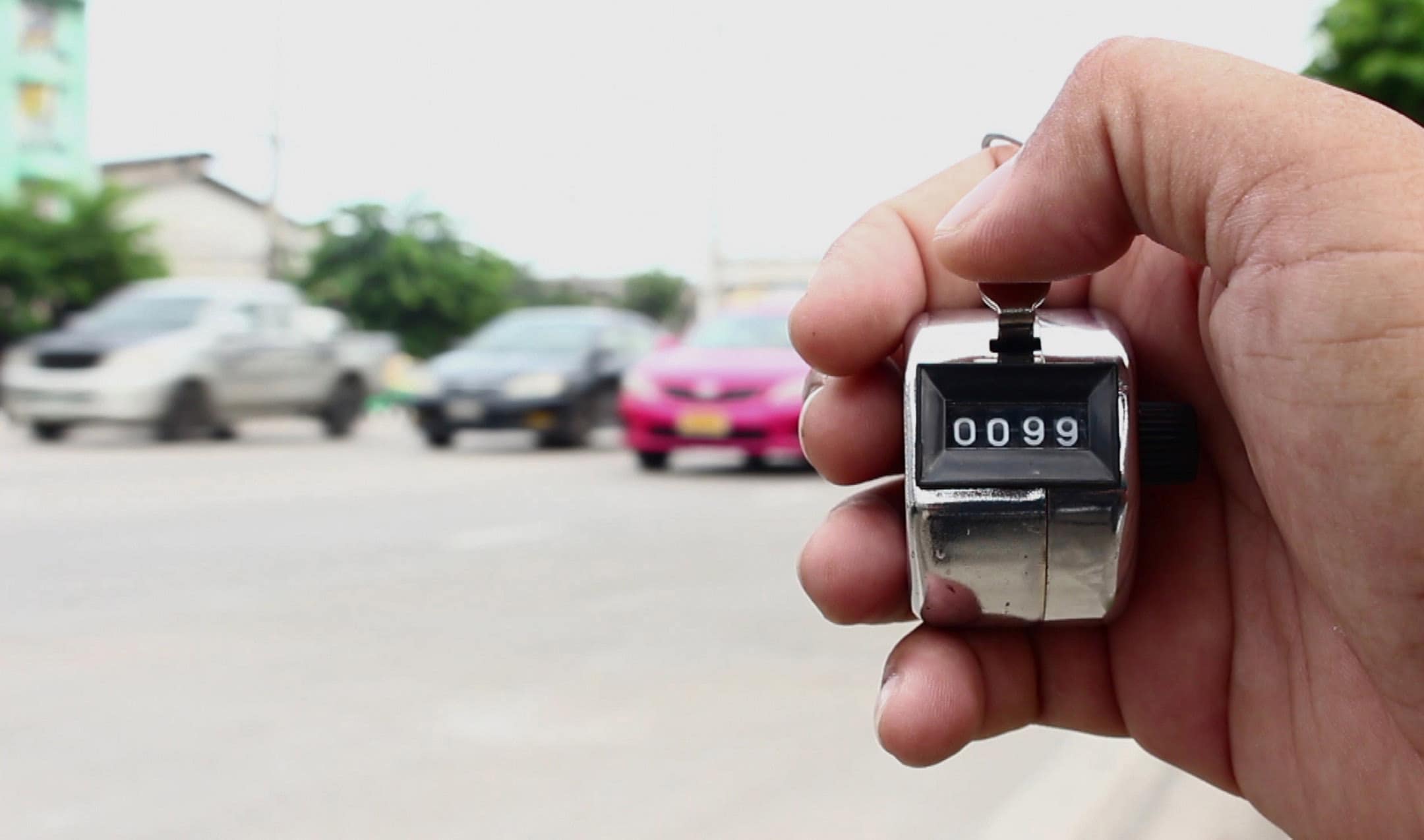 Hand holding a mechanical counter showing "0099" with blurred cars in the background on a street.