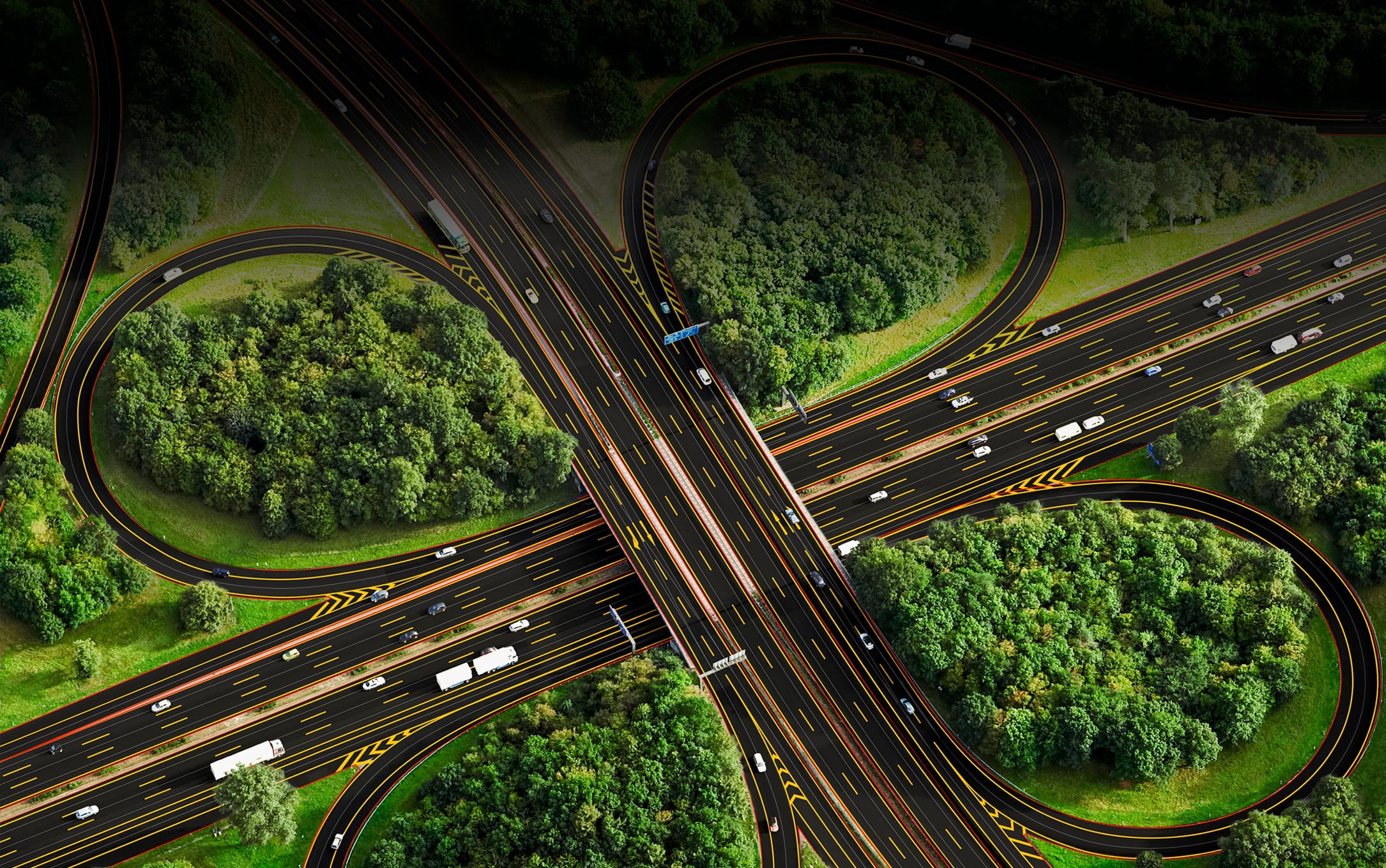 Aerial view of a highway interchange surrounded by dense green trees, featuring multiple lanes and vehicles in motion.