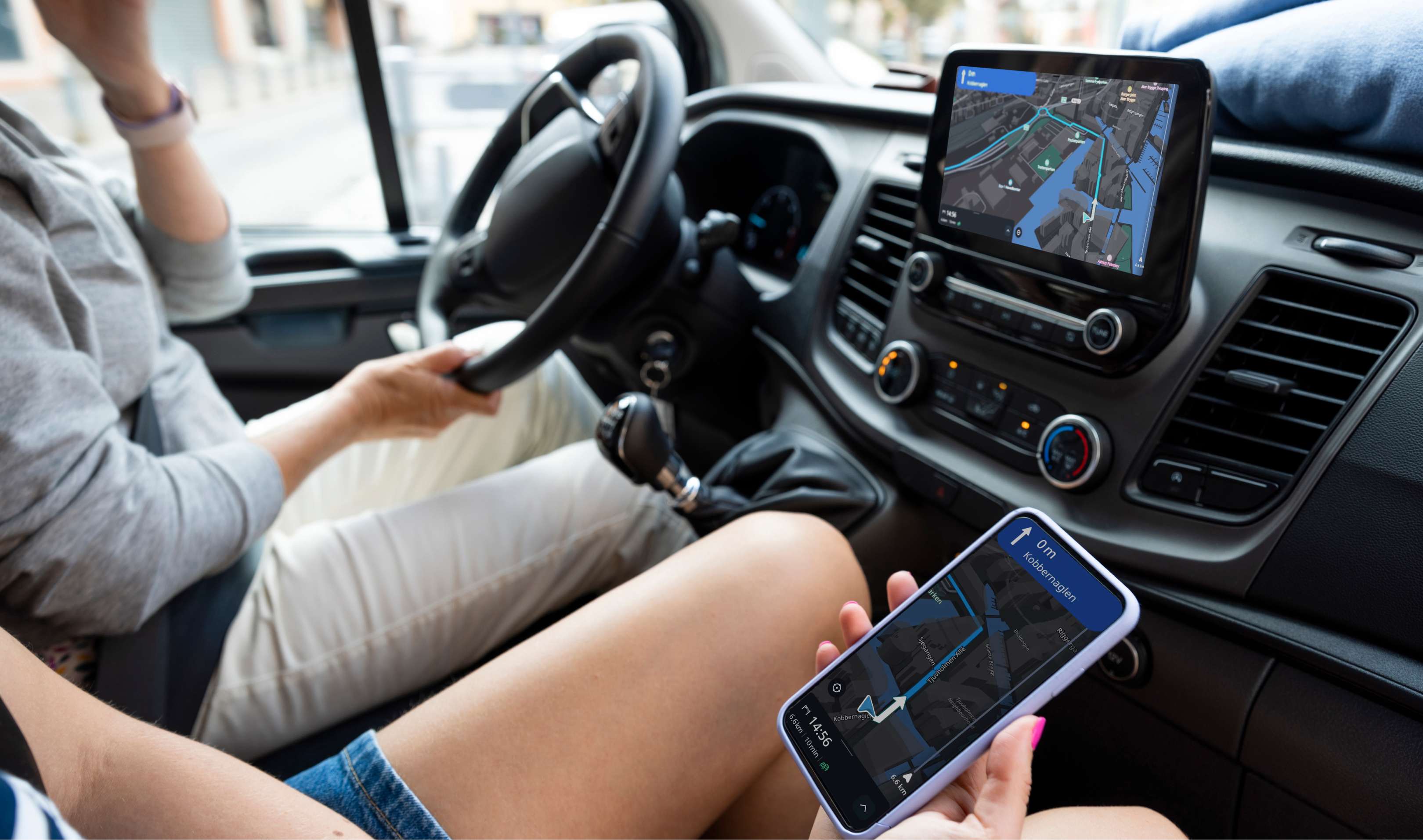 Person driving a car using GPS navigation on a dashboard tablet while a passenger holds a phone with the same map displayed.