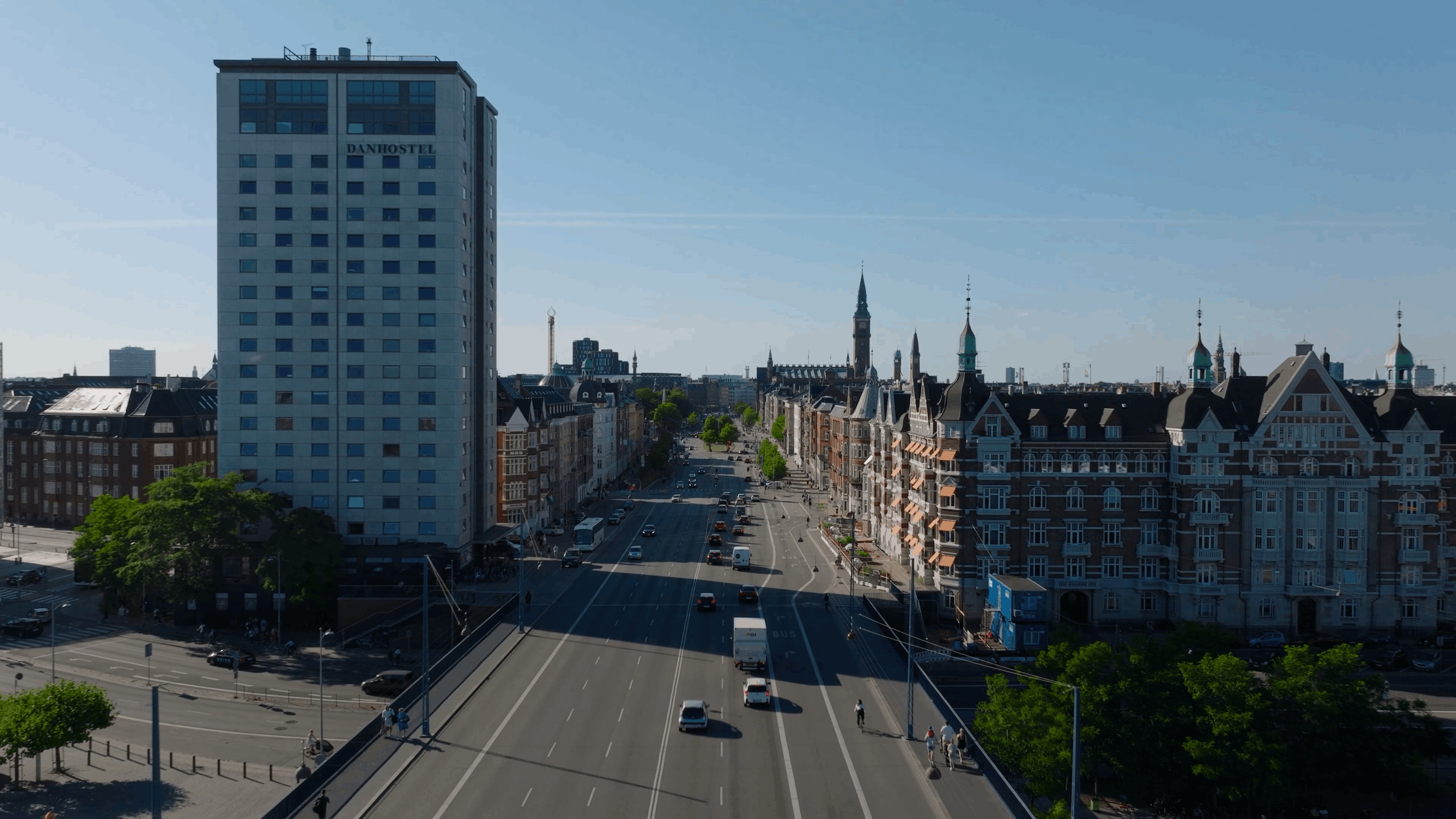 City street view with a tall building on the left labeled "Danhostel," lined with historic buildings and light traffic under a clear blue sky.