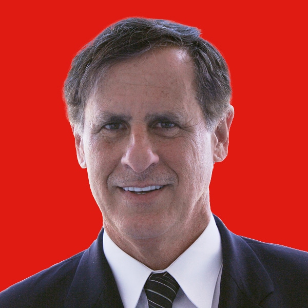 Smiling man in a suit and tie, with a red background.