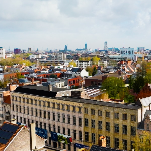 Aerial view of a European cityscape with a mix of historical and modern buildings, greenery, and a cloudy sky in the background.